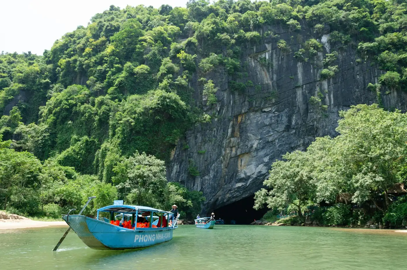 Trekkers wading along a river inside Hang En cave beneath a large natural skylight opening, Phong Nha-Ke Bang, Vietnam