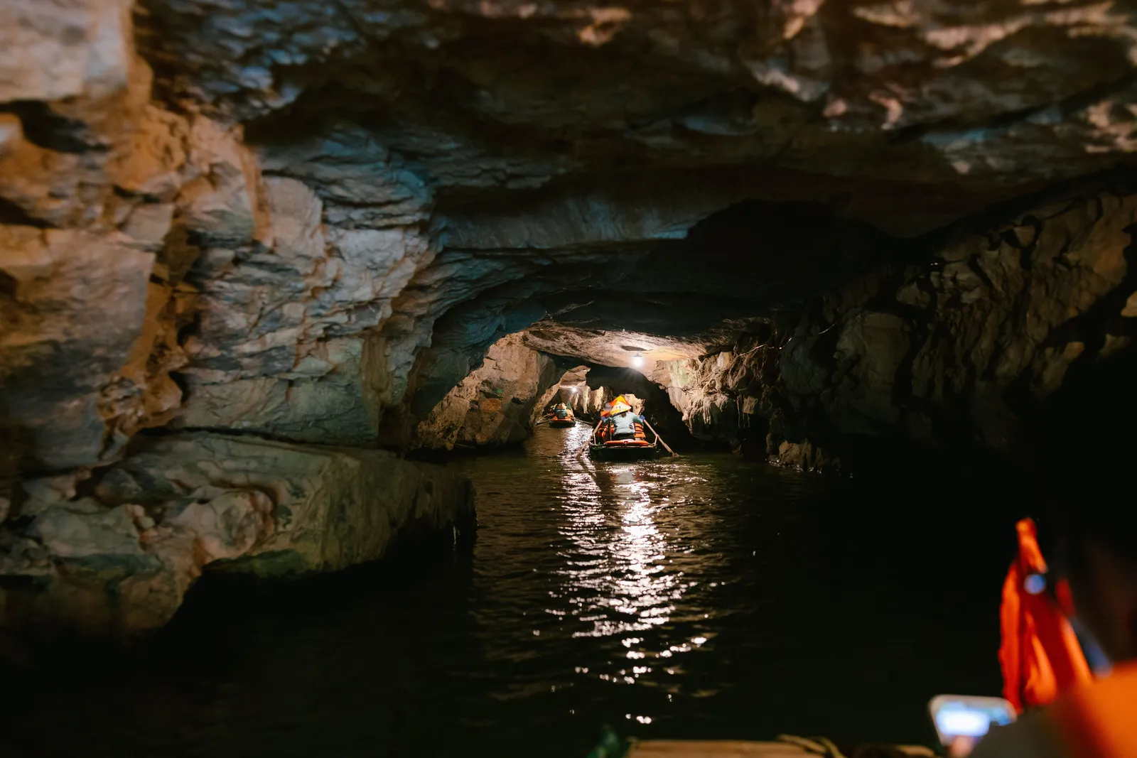 A local rower steering a small boat with her feet beneath a low cave tunnel at Tam Coc, Ninh Binh