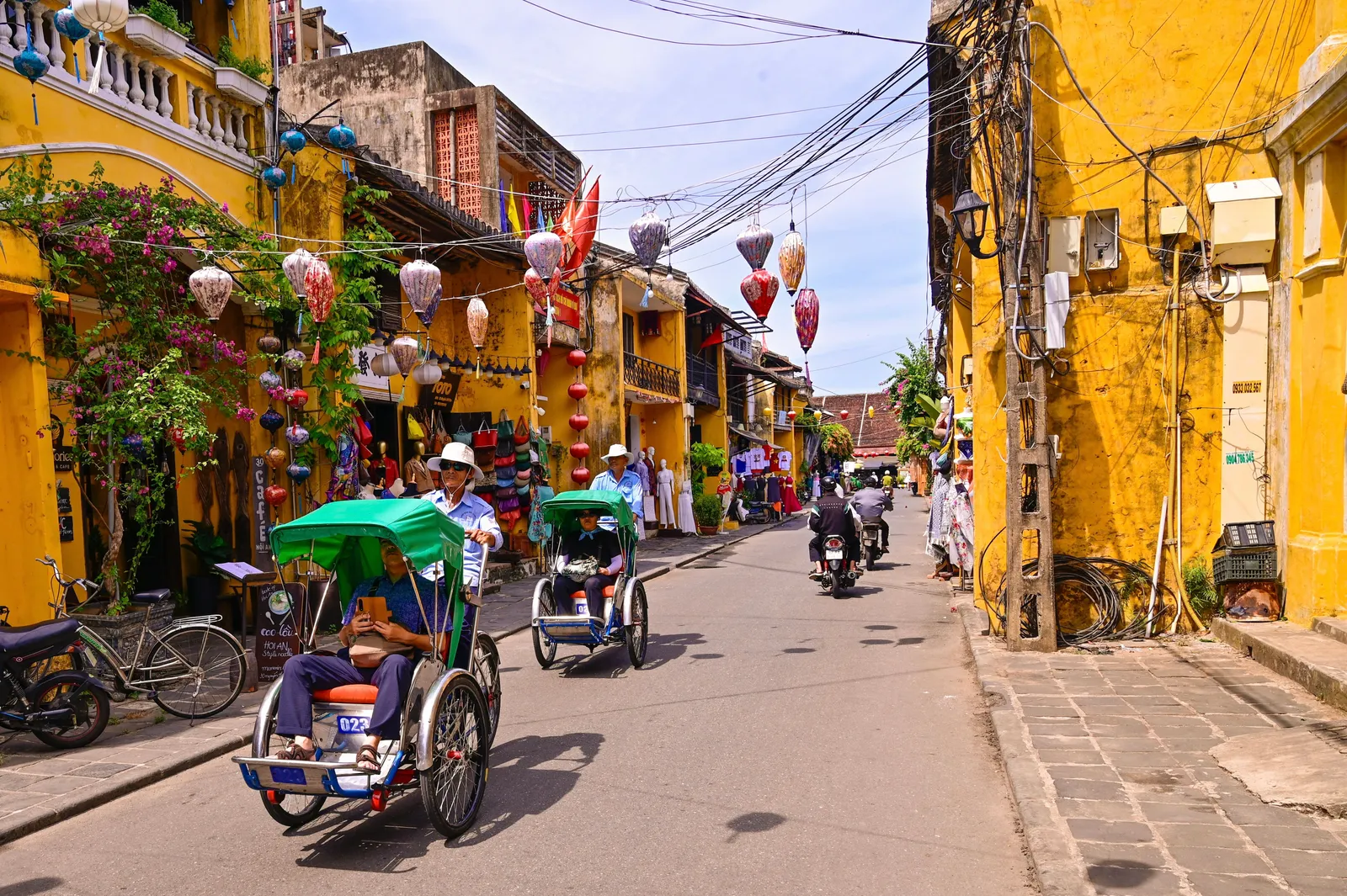 Lantern-lit shopfronts and yellow walls along a street in the old town of Hoi An, Vietnam, in the late afternoon