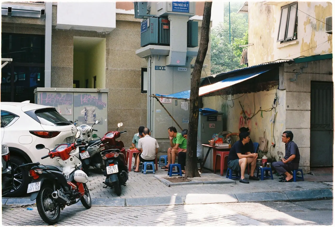 Locals sitting on low plastic stools at a street corner in Hanoi, Vietnam