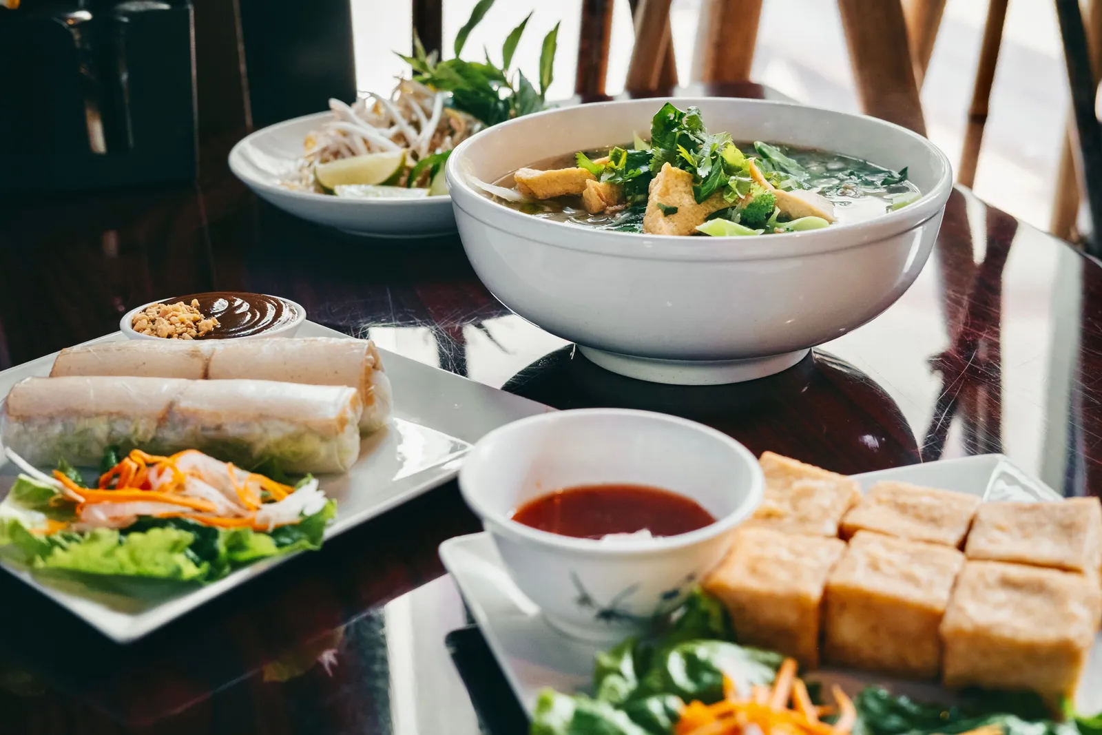 Bowls of noodle soup and fresh spring rolls on a table at a Vietnamese restaurant