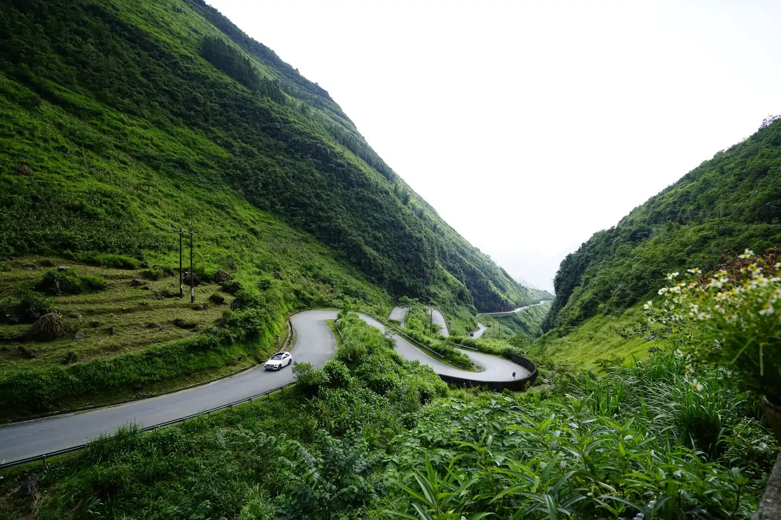 A vehicle on a winding mountain road through the green landscape of northern Vietnam