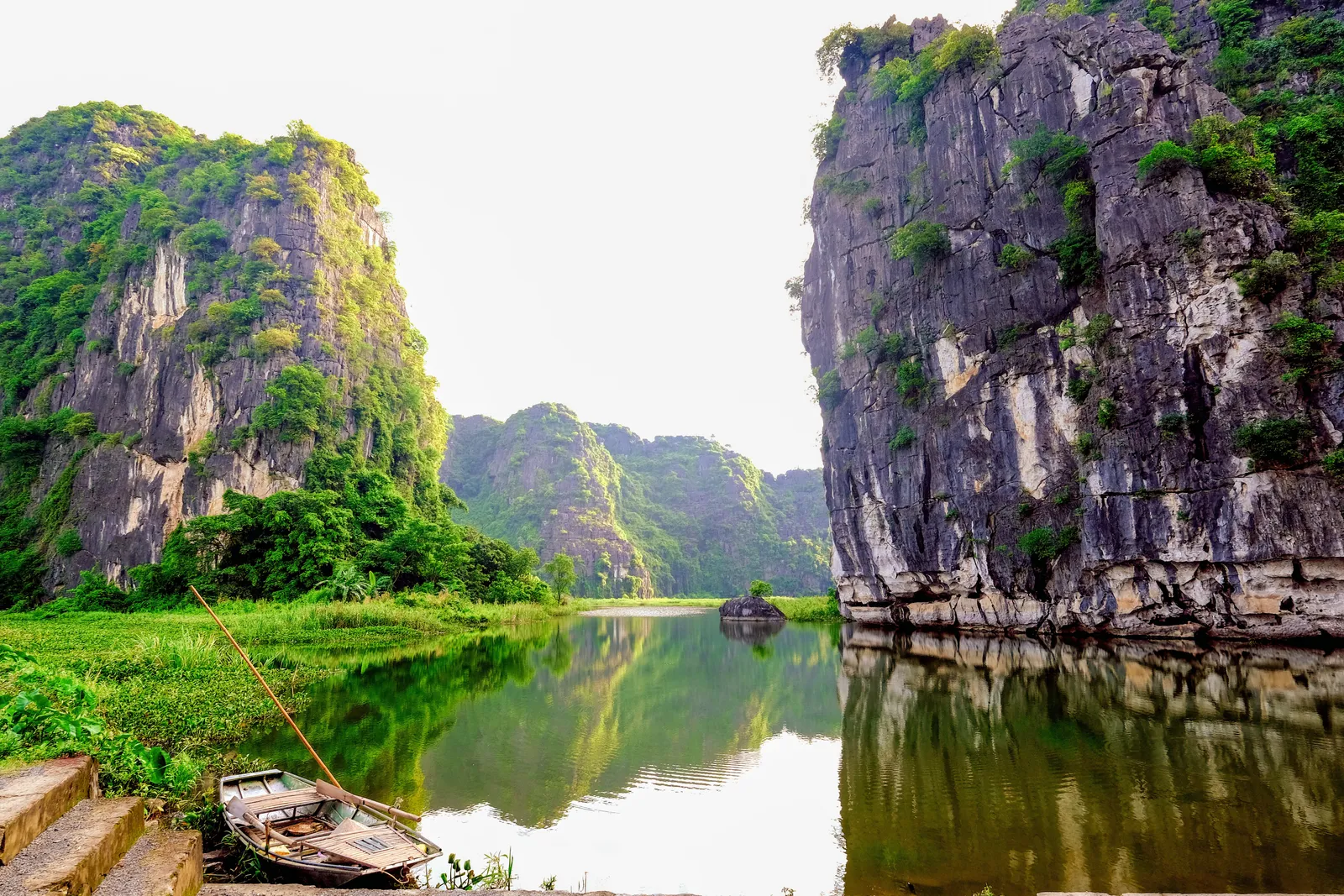 A wooden sampan moored on the river between towering limestone karsts at Tam Coc, Ninh Binh, Vietnam