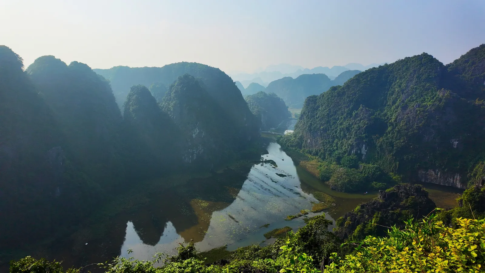 Limestone karst peaks rising above green rice fields and a winding river at Tam Coc in Ninh Binh, Vietnam, in daylight