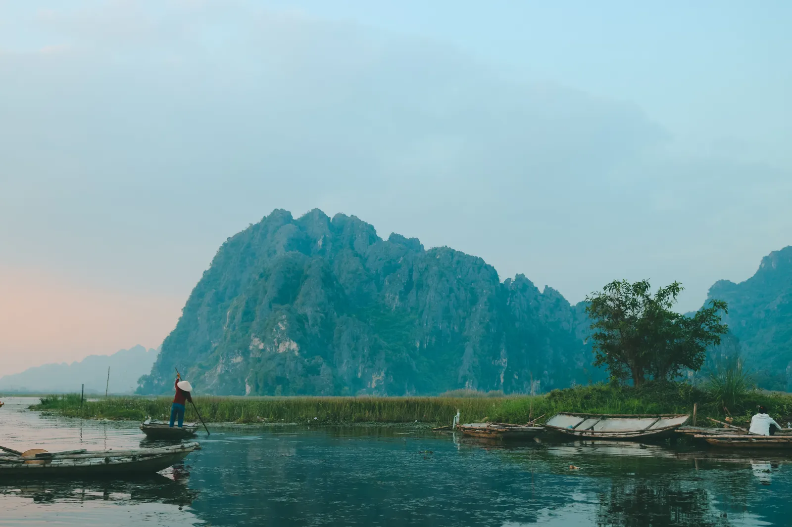 Limestone karsts rising from calm water at dawn in northern Vietnam with a traditional boat in the foreground