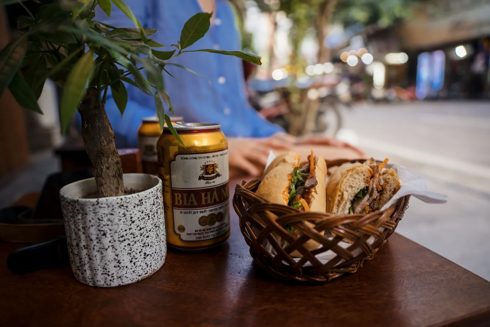Cans of Vietnamese beer beside a basket of banh mi on a street side table in Vietnam