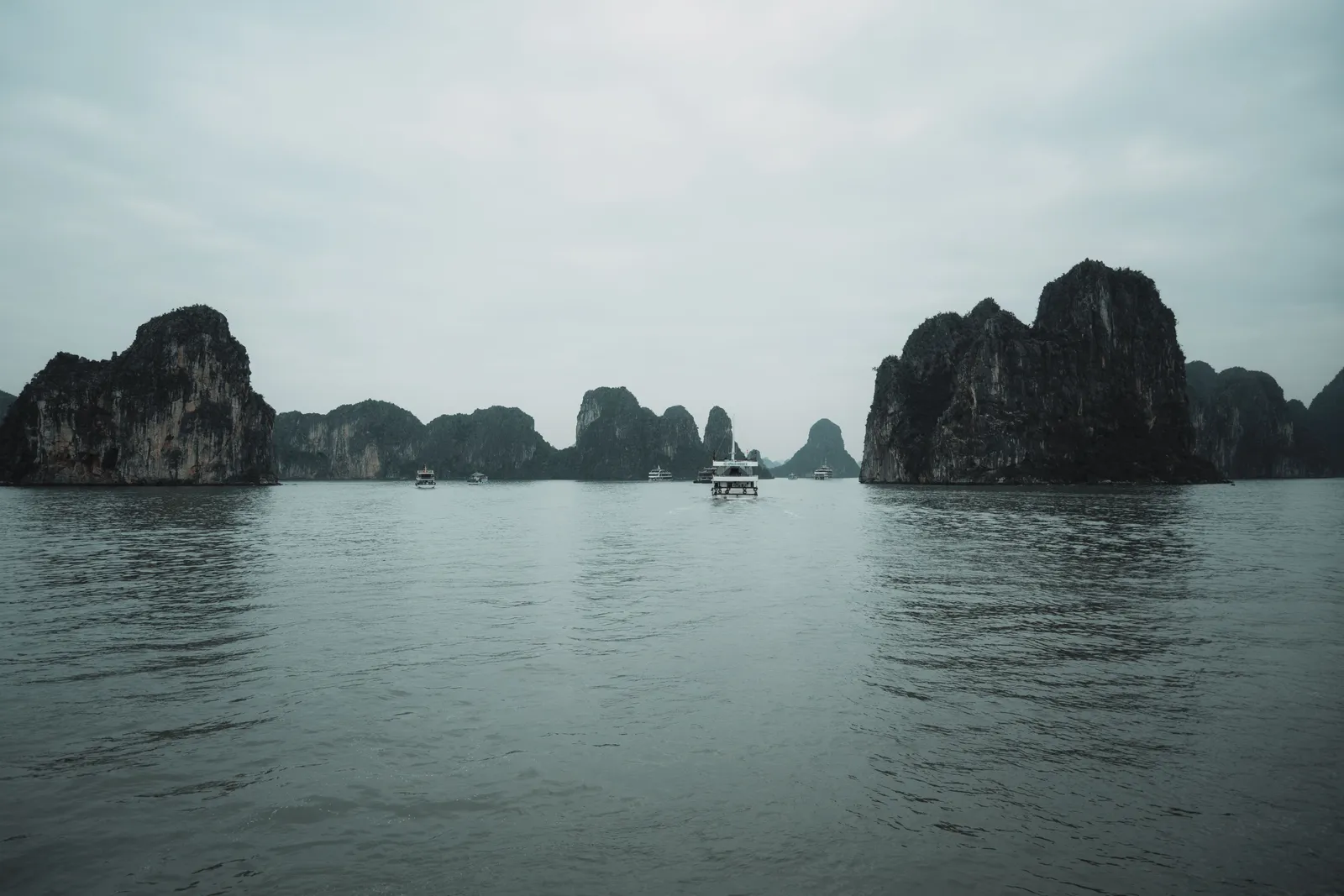 A traditional junk boat anchored among limestone karsts at sunset in a northern Vietnamese bay