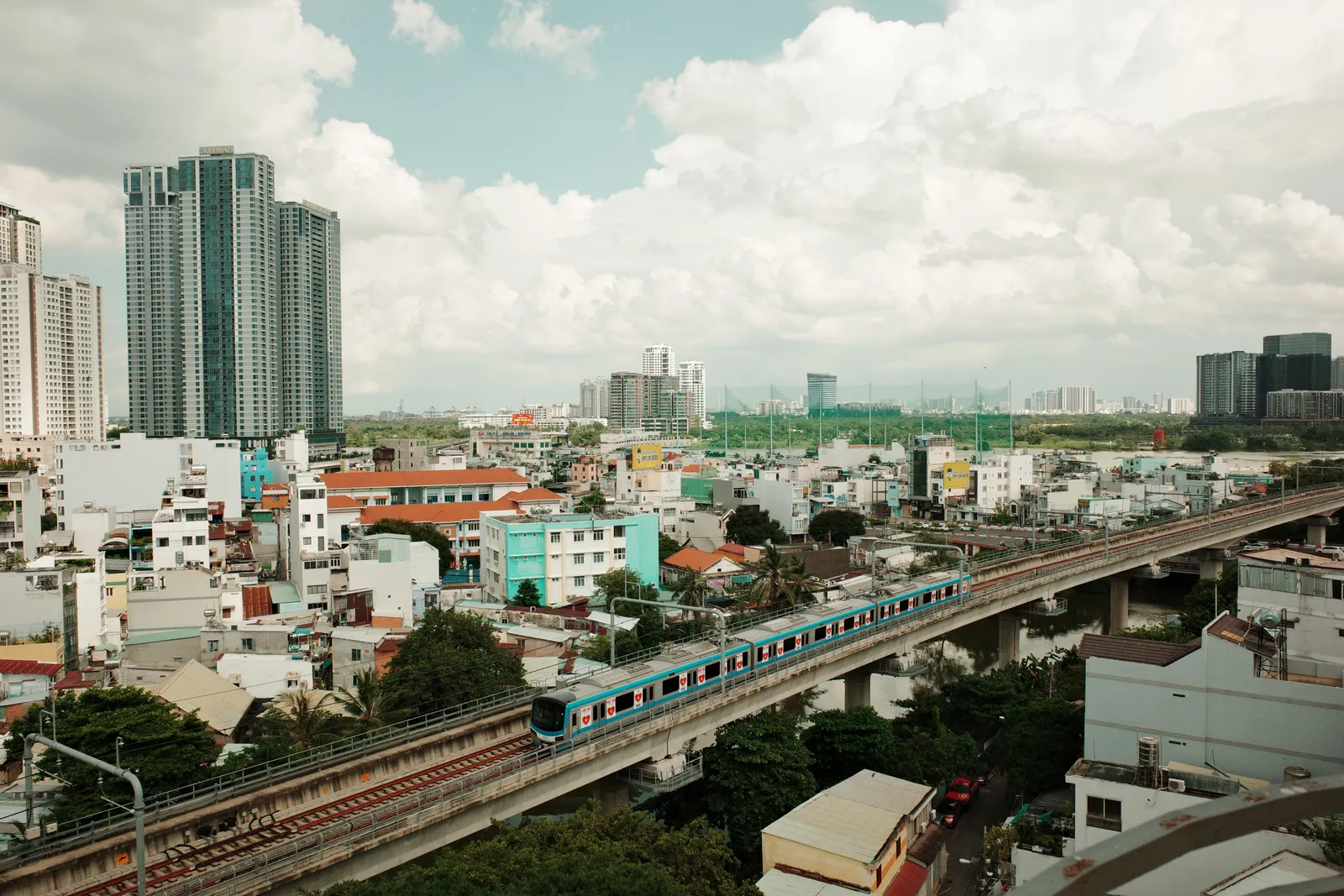 A modern elevated metro train crossing above a busy road in Ho Chi Minh City, Vietnam, in daylight