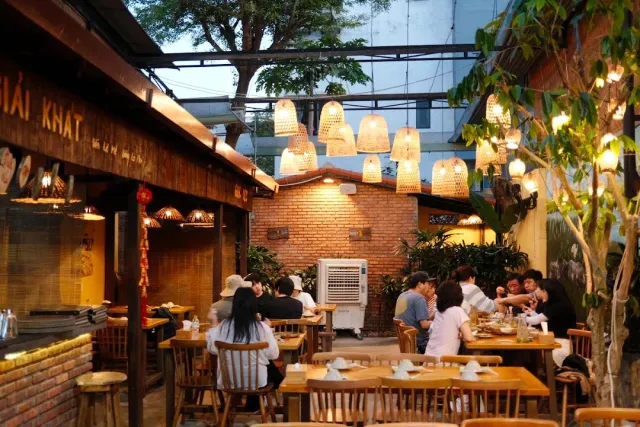 A seating courtyard with woven bamboo lampshades hanging, brick walls and wooden tables