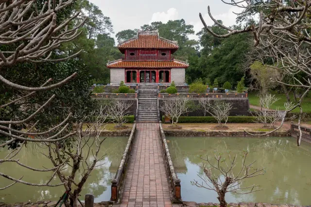An imperial pavilion with a tiled roof at the end of a stone bridge over a lake