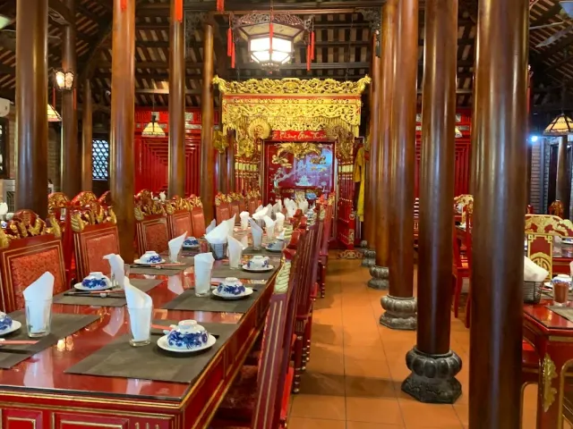 A traditional wooden hall with dark columns, a carved gilded partition and set red tables