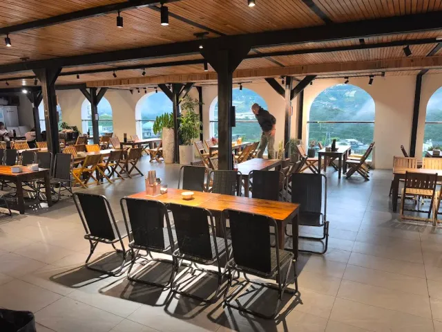 A wide hall with a wooden ceiling, arched openings framing a mountain view and folding chairs