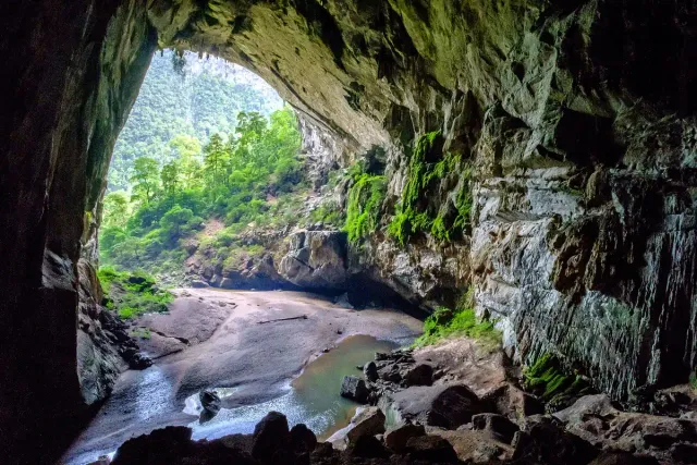 An enormous cave mouth framing forest and a stream inside it