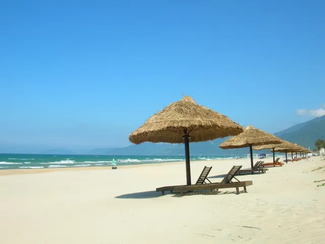 Thatched parasols and loungers on pale sand facing a turquoise sea