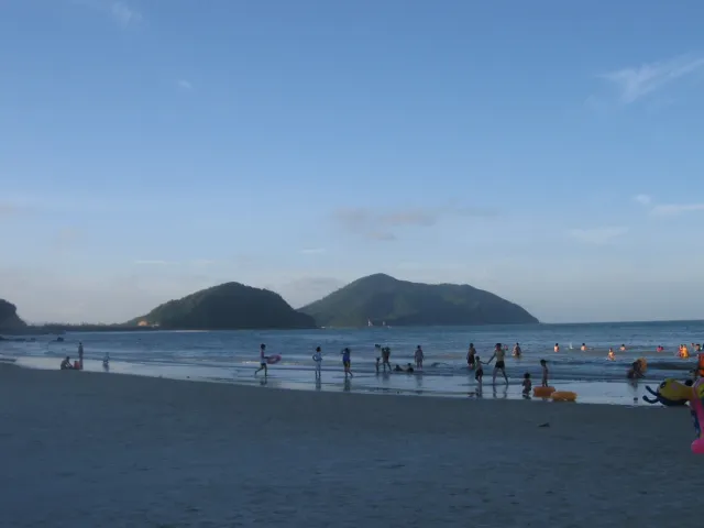 A sandy beach with calm sea and a green hill rising beyond the water