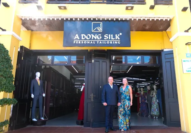 An entrance in a yellow building with dark wooden doors open, a couple and mannequins at the doorway