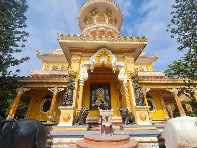 A yellow and white pagoda with a rounded dome, an ornate portal and black lion statues at the entrance