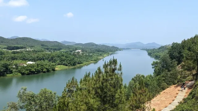 A green river curving between forested hills, pine trees and a dirt path in front