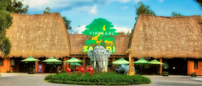 An entrance with thatched roofs, a large elephant sculpture and colourful animal figures in the garden in front