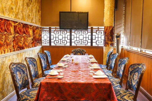 A private room with a long table in a red cloth, chairs upholstered in blue and gold and a screen on the wall