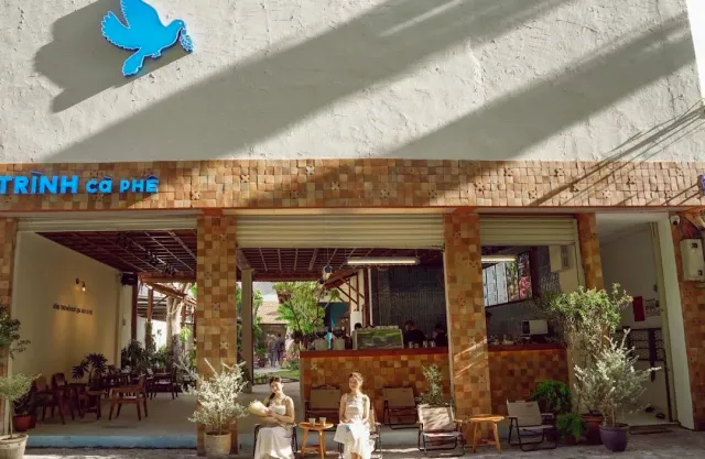 A white building with a blue dove sculpture, brick pillars and two women seated at the open entrance