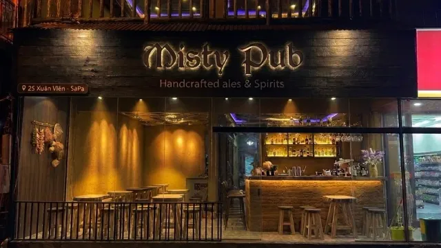 A dark wooden facade at night with a lit golden sign and a bar counter open to the street