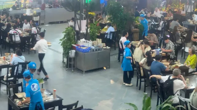 A large dining hall full of diners, with waiters in light blue uniforms between the tables