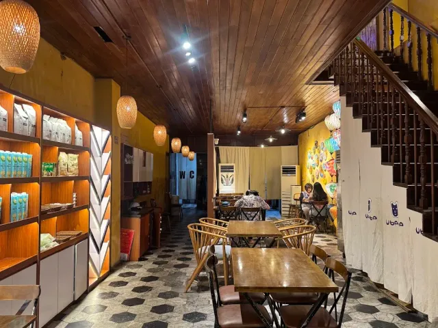 A narrow space with a wooden ceiling, straw lamps, lit product shelves and wooden stairs at the side