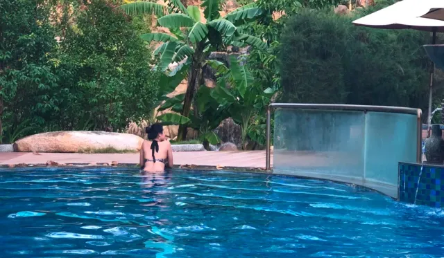 A large blue pool surrounded by banana trees and rocks, a traveler bathing at the edge