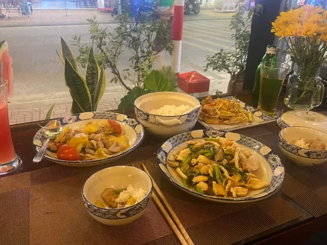 A set table with stir fried dishes, rice bowls and drinks facing a window onto the street