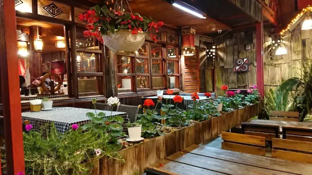 A wooden interior with checkered cloths, boxes of red flowers and a hanging planter above the tables