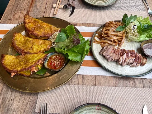 A brass tray with three folded yellow pancakes and dipping sauce, beside a plate of sliced meat