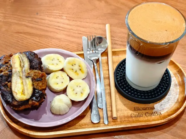 A banana pancake, banana slices and a layered iced coffee on a wooden tray