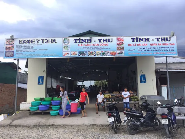An open restaurant front with a colorful sign, plastic tubs and parked motorbikes