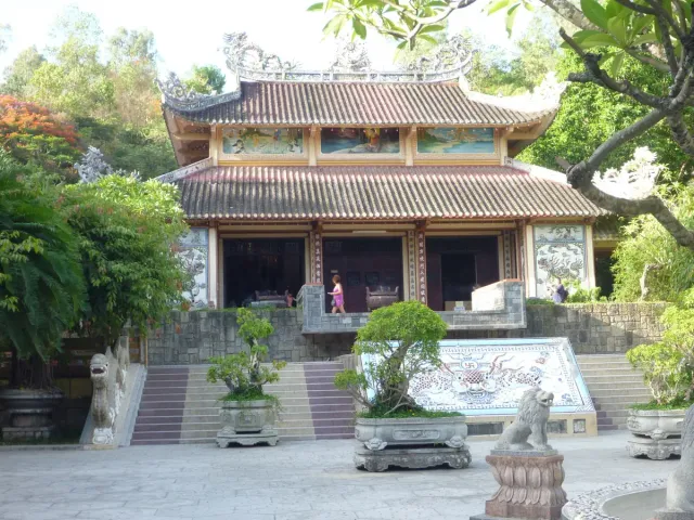 A temple building with a red tiled roof, a garden and a pool in front