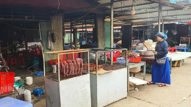 Covered stalls with a display case of hanging sausages, a woman in traditional blue dress