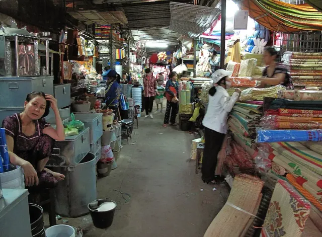 A narrow aisle in a covered market with fabric stalls and a vendor