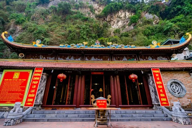 A hall facade with a dragon decorated roof ridge, red signboards and a limestone cliff behind