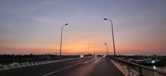 A wide road on a bridge with street lamps, under orange skies at twilight