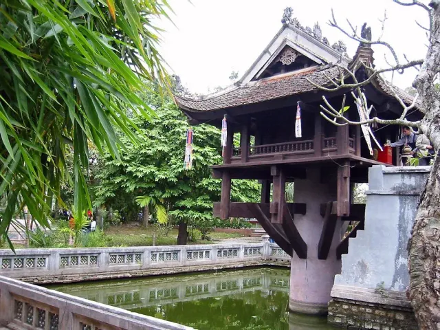 A small wooden pavilion on a single pillar above a pond, surrounded by greenery