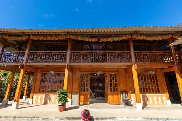 A two storey wooden building with a carved balcony and corn bunches hanging under the roof