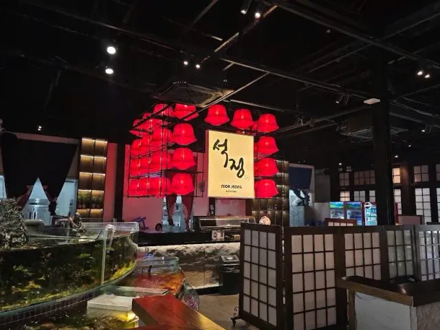 A dim space with a cluster of red lamps, a lit sign, aquariums and wooden lattice partitions