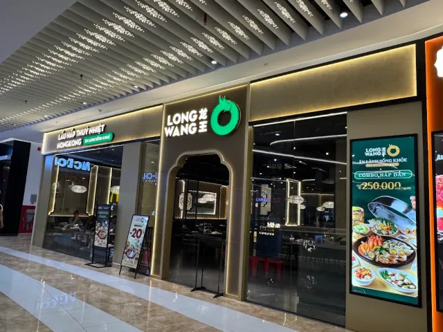 A mall storefront with a green neon logo, dark glass and a lit menu screen showing dishes