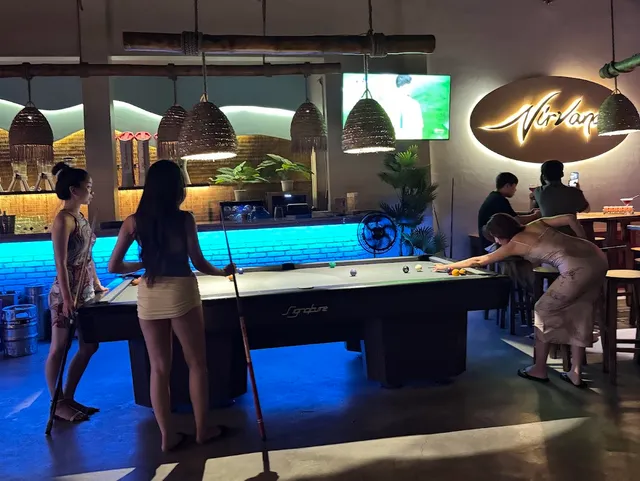 A pool table in a blue lit bar, with an illuminated sign on the wall