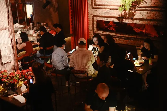 A dim bar with a brick wall, a red curtain and diners at small tables