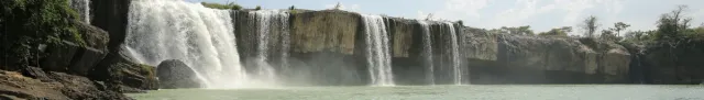 A wide waterfall dropping from a rock shelf across the full width of the frame