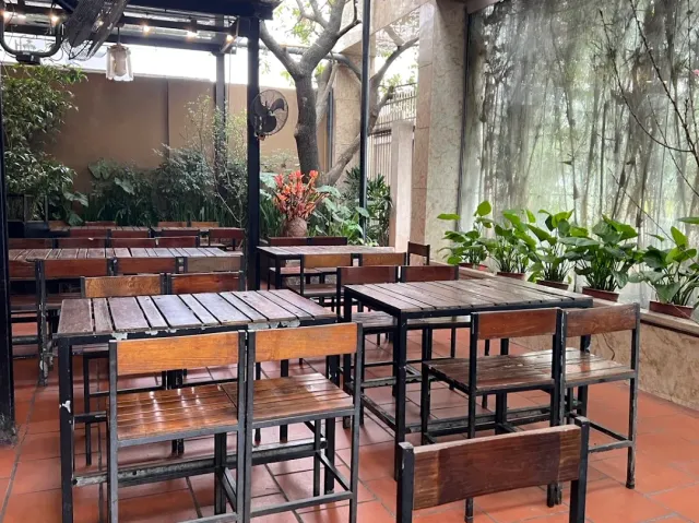 A covered patio with wooden tables and stools, a terracotta floor and greenery behind glass