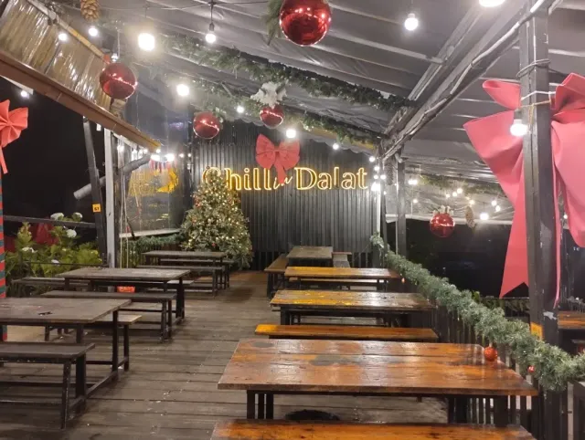 A covered terrace in the evening with long wooden tables, holiday decorations, red baubles and lights