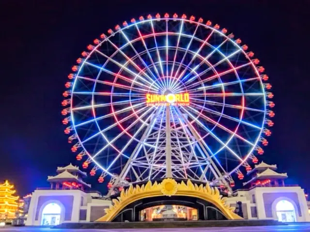 A giant circular ride lit at night in red and blue lights, above a gilded gate
