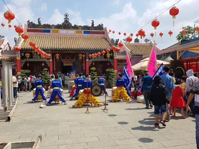 A temple courtyard strung with red lanterns, a lion dance troupe in blue costumes and a crowd